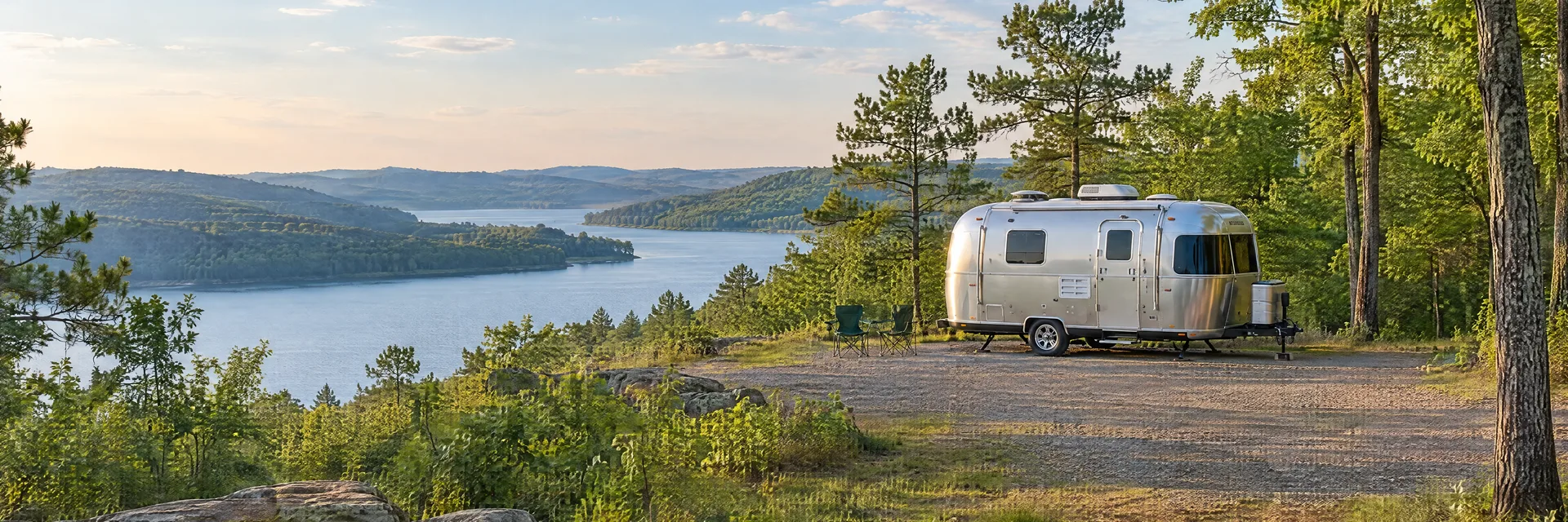 Illustration of a rounded silver travel trailer at a fictional camping setting inspired by Bella Vista, AR.