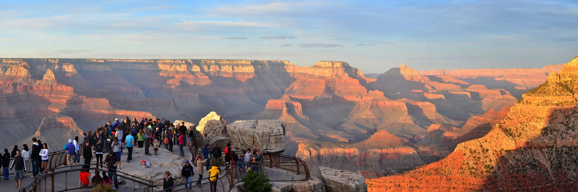Visitors at Mather Point overlooking Grand Canyon in golden sunset light.