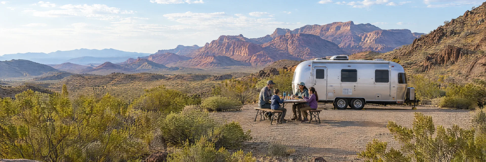 Illustration of campers enjoying a family picnic beside a rounded silver travel trailer in a fictional camping setting inspired by Littlefield, AZ.