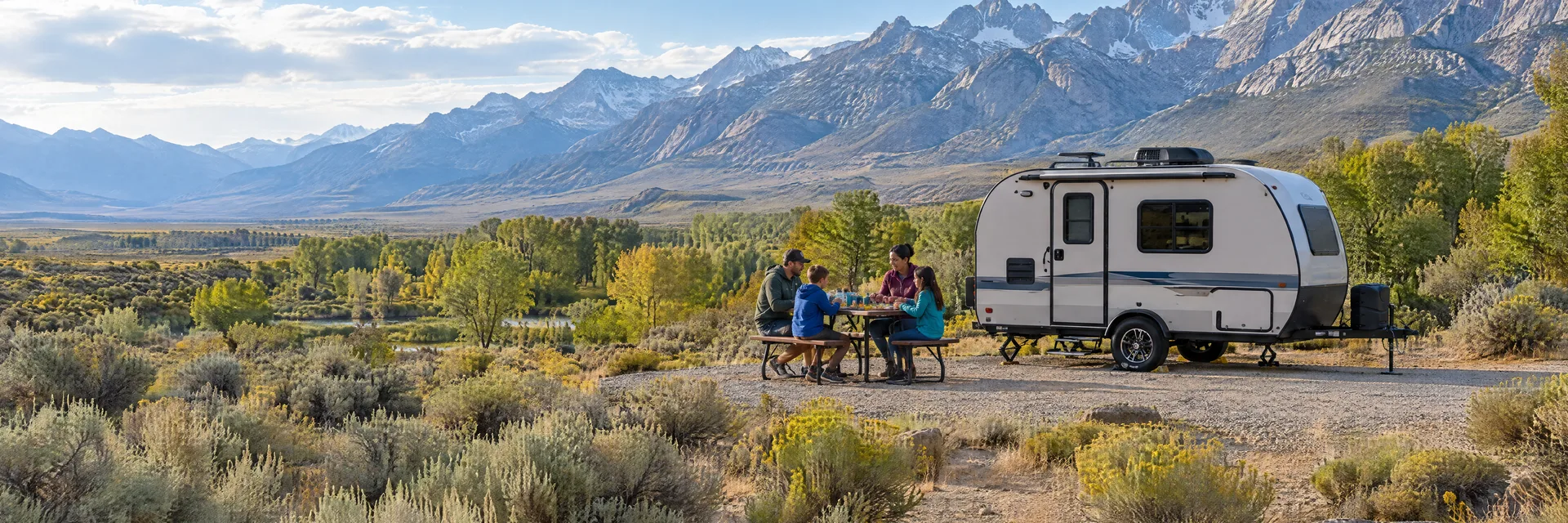 Illustration of campers enjoying a family picnic beside a compact travel trailer in a fictional camping setting inspired by Big Pine, CA.