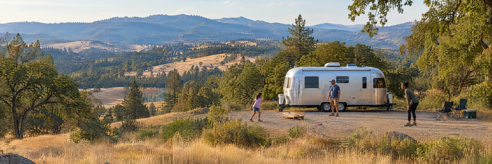 Illustration of campers enjoying family campsite activities beside a rounded silver travel trailer in a fictional camping setting inspired by Bootjack, CA.