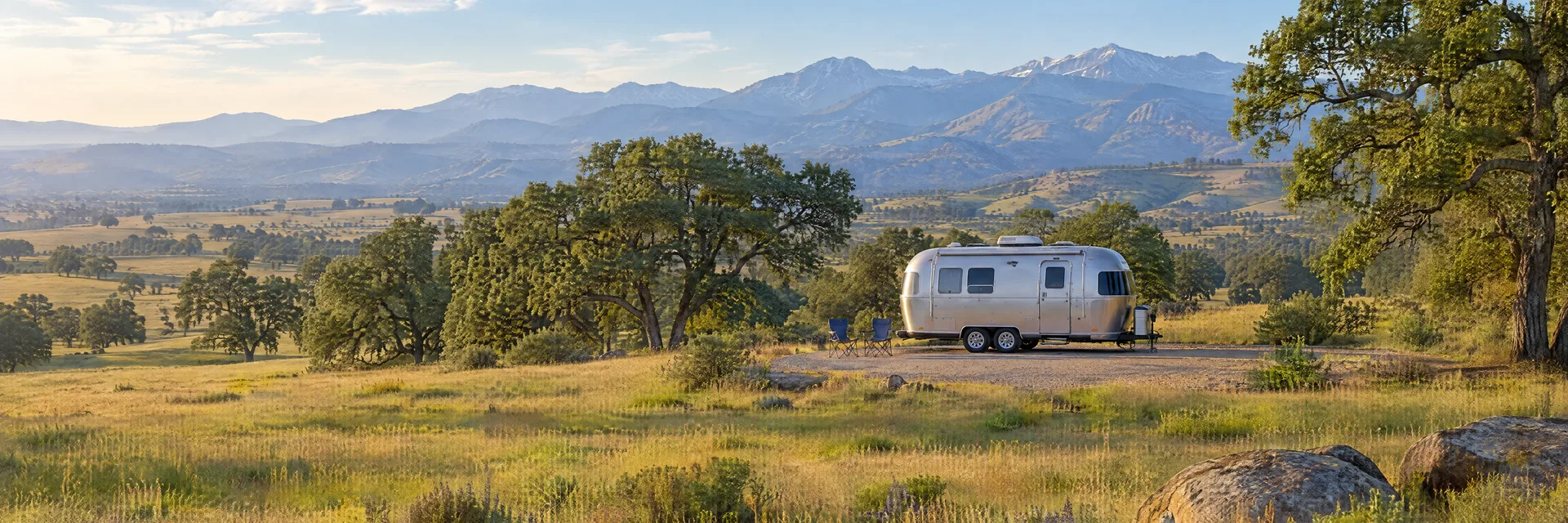 Illustration of a rounded silver travel trailer at a fictional camping setting inspired by Merced, CA.