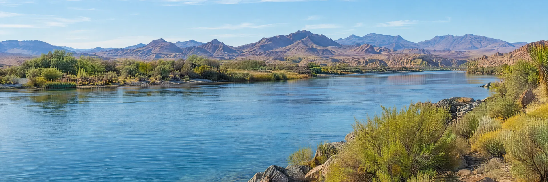 Illustration inspired by Needles, CA: california Mojave desert river shore with blue water, sparse desert scrub and distant mountains.