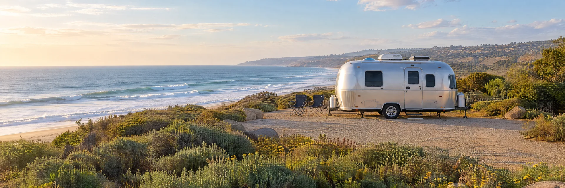 Illustration of a rounded silver travel trailer at a fictional camping setting inspired by Oceanside, CA.