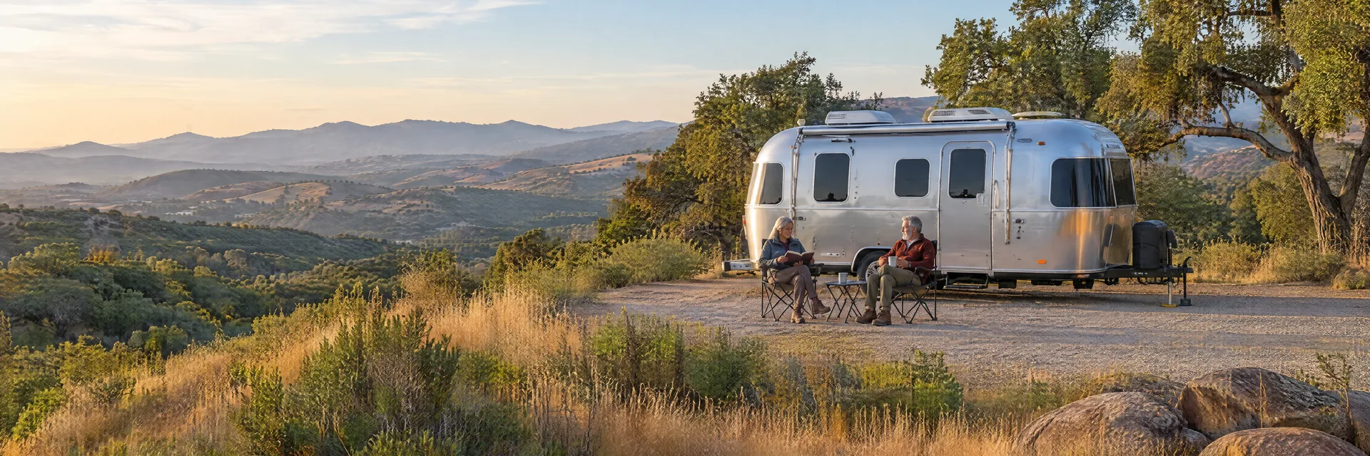Illustration of campers enjoying relaxing at camp beside a rounded silver travel trailer in a fictional camping setting inspired by Vista, CA.