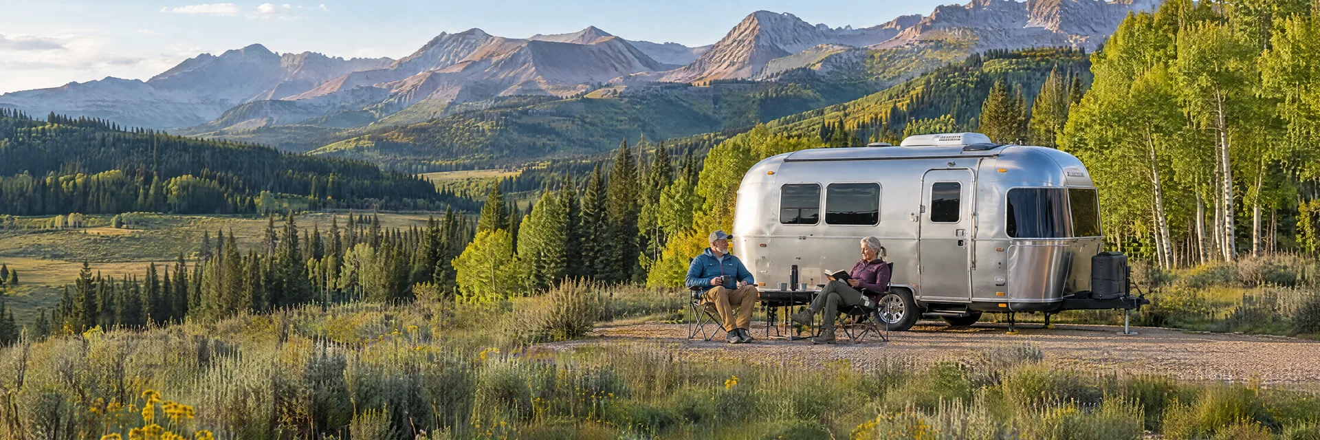 Illustration of campers enjoying relaxing at camp beside a rounded silver travel trailer in a fictional camping setting inspired by Crested Butte, CO.