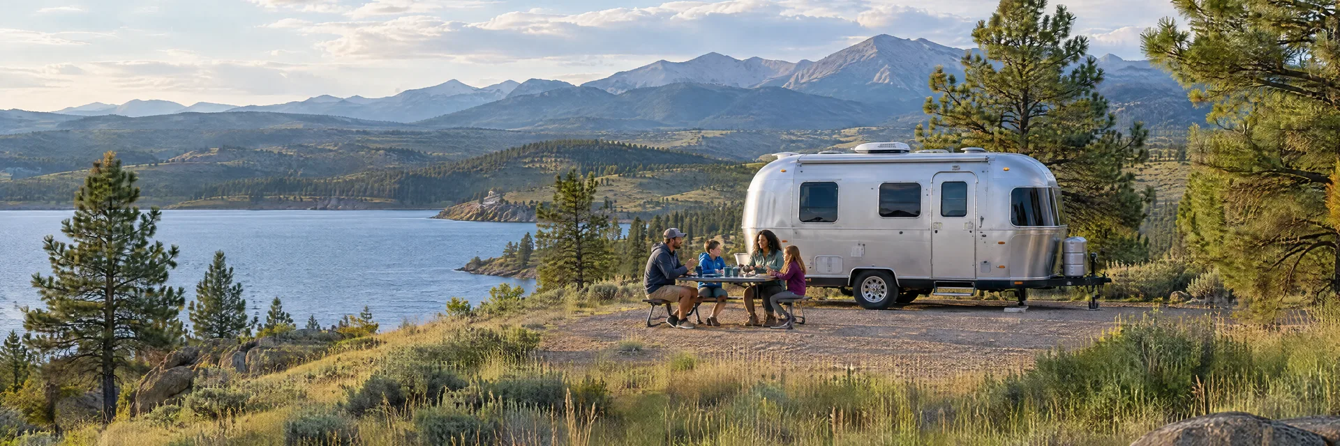 Illustration of campers enjoying a family picnic beside a rounded silver travel trailer in a fictional camping setting inspired by Fort Collins, CO.