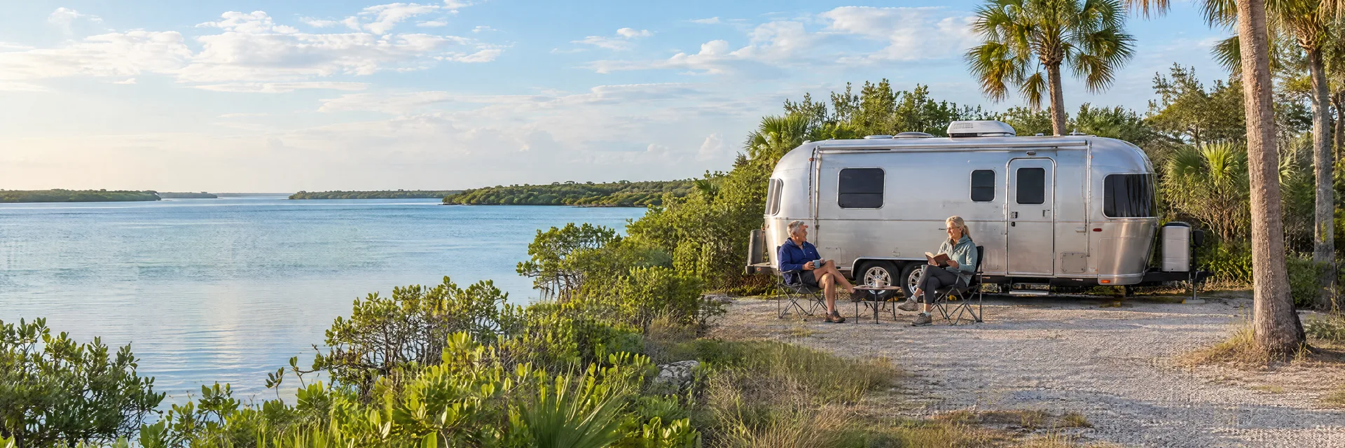 Illustration of campers enjoying relaxing at camp beside a rounded silver travel trailer in a fictional camping setting inspired by Englewood, FL.