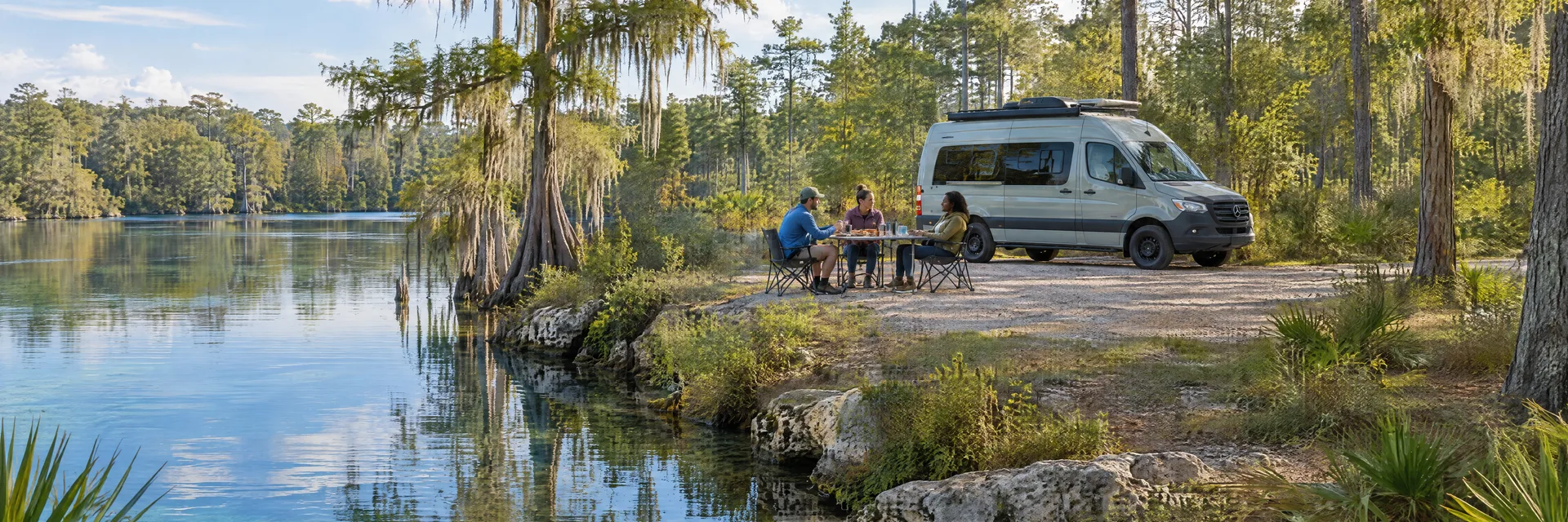 Illustration of campers enjoying an outdoor meal beside a camper van in a fictional camping setting inspired by Marianna, FL.