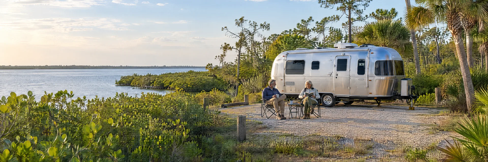 Illustration of campers enjoying relaxing at camp beside a rounded silver travel trailer in a fictional camping setting inspired by North Fort Myers, FL.