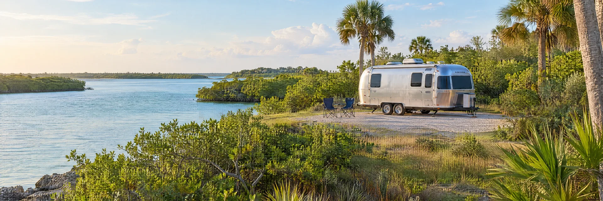 Illustration of a rounded silver travel trailer at a fictional camping setting inspired by Osprey, FL.