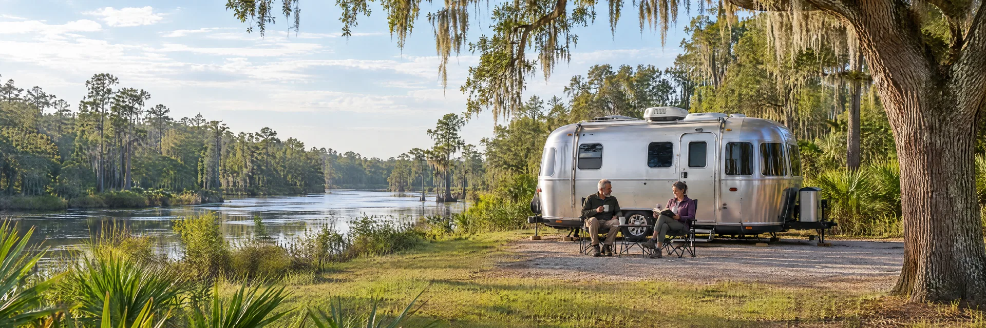 Illustration of campers enjoying relaxing at camp beside a rounded silver travel trailer in a fictional camping setting inspired by Ridge Manor, FL.