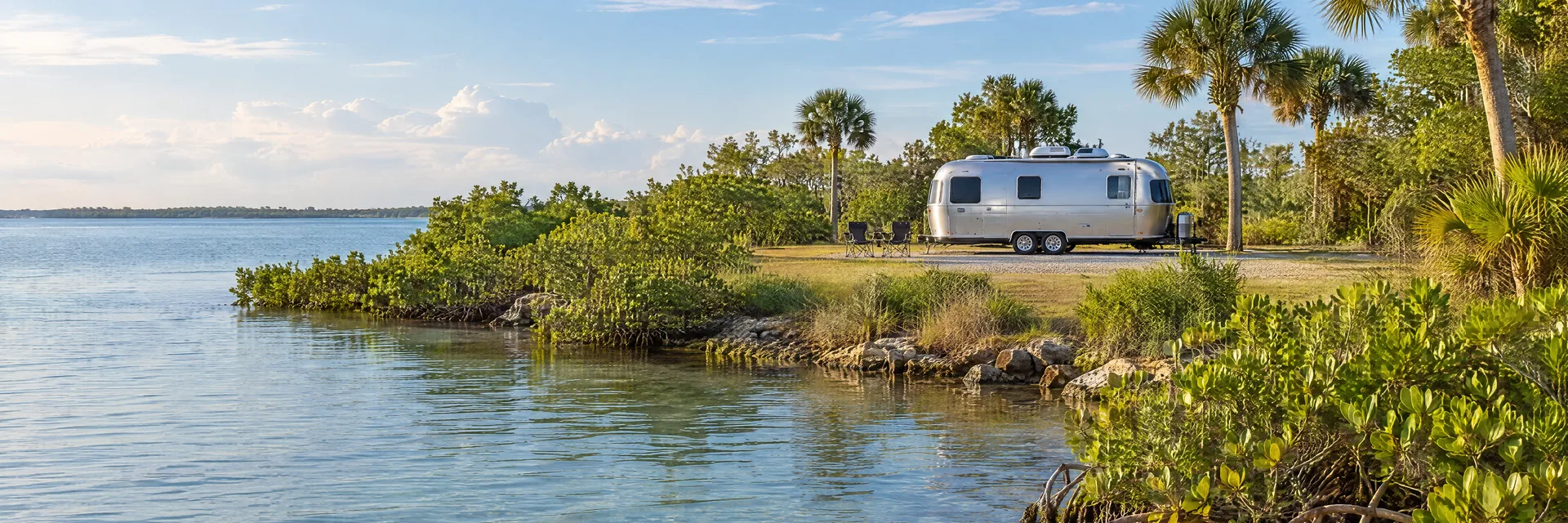 Illustration of a rounded silver travel trailer at a fictional camping setting inspired by Ruskin, FL.