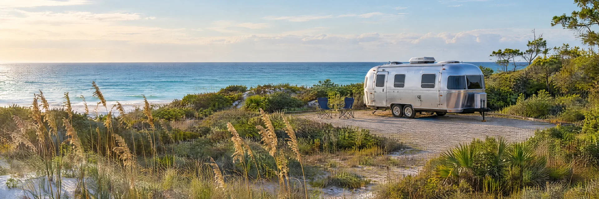Illustration of a rounded silver travel trailer at a fictional camping setting inspired by Santa Rosa Beach, FL.