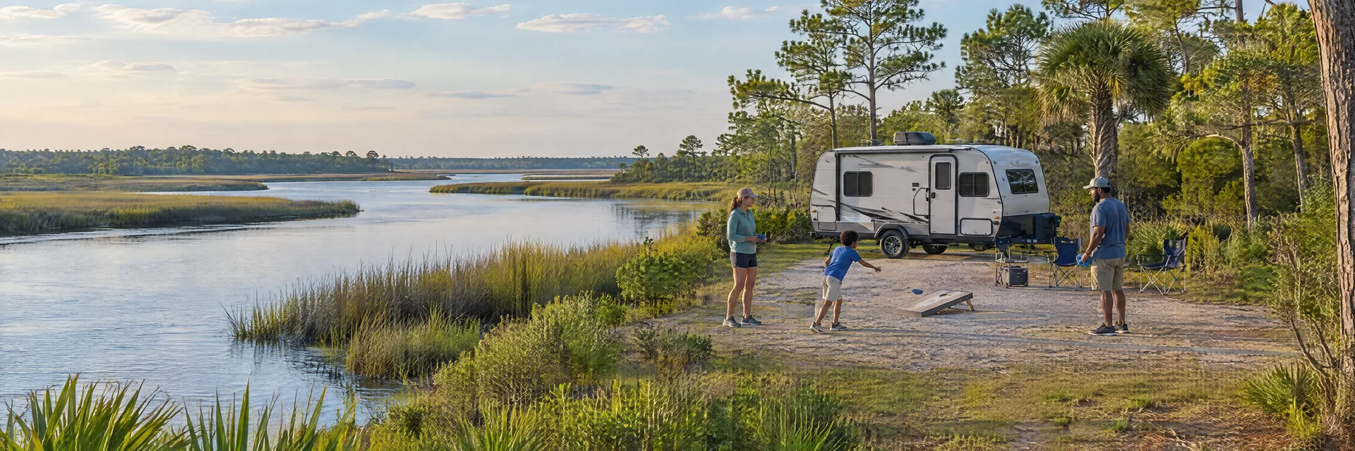 Illustration of campers enjoying family campsite activities beside a compact travel trailer in a fictional camping setting inspired by Steinhatchee, FL.