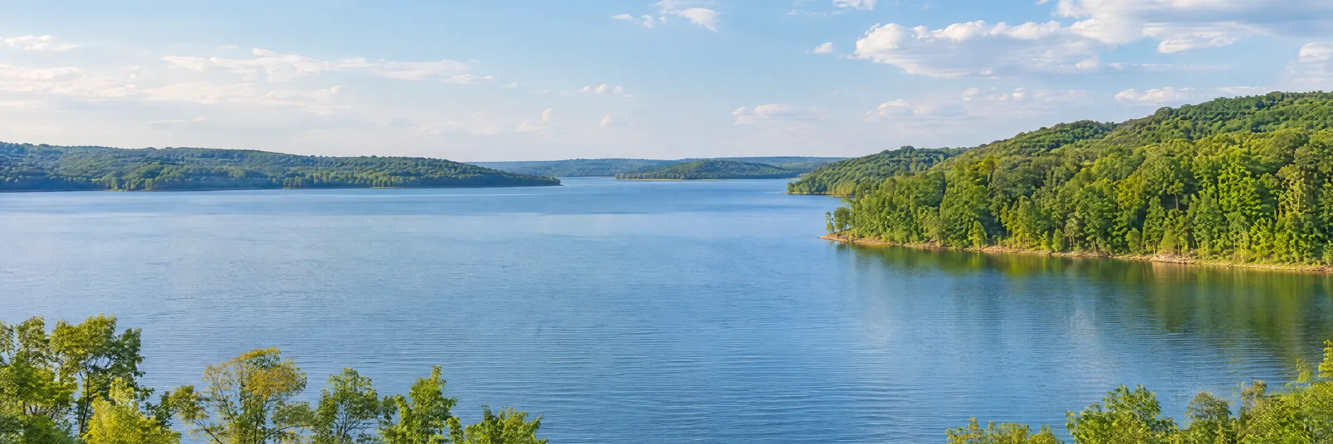 Illustration inspired by Monticello, IN: north-central Indiana lake country, broad blue reservoir, leafy deciduous shoreline and gently rolling green hills.