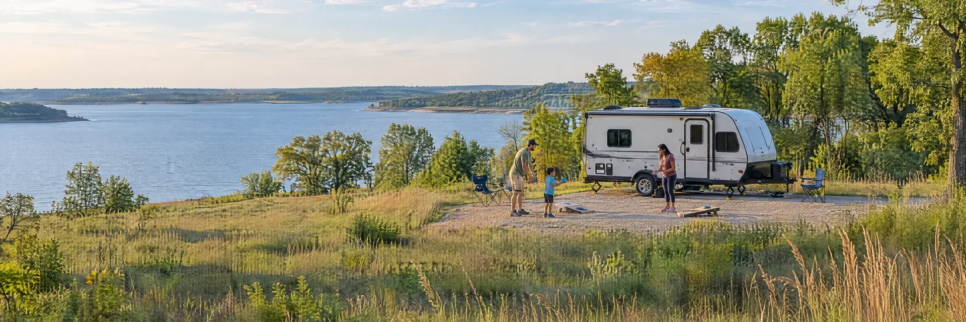 Illustration of campers enjoying family campsite activities beside a compact travel trailer in a fictional camping setting inspired by Lawrence, KS.