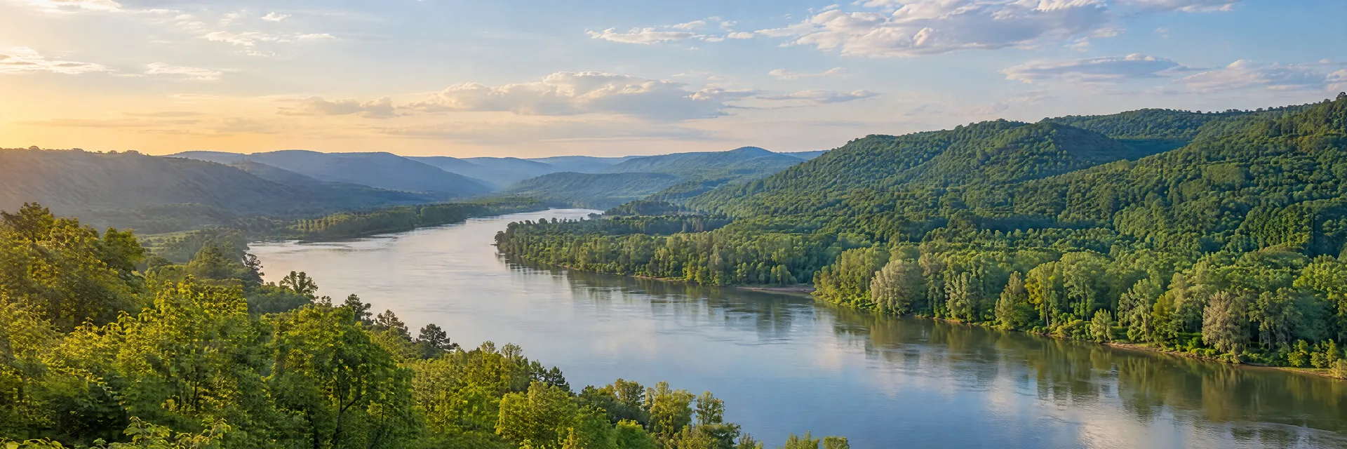 Illustration inspired by Ashland, KY: northeastern Kentucky broad river valley with green wooded hills and leafy riverbank groves.