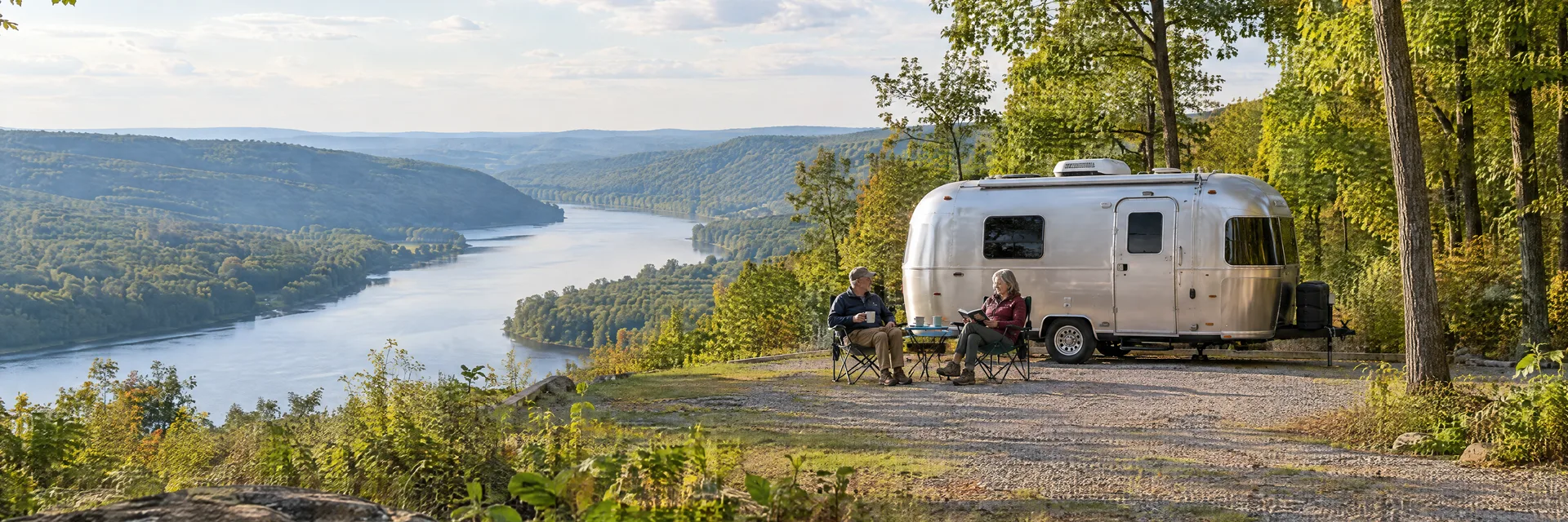 Illustration of campers enjoying relaxing at camp beside a rounded silver travel trailer in a fictional camping setting inspired by Little Orleans, MD.