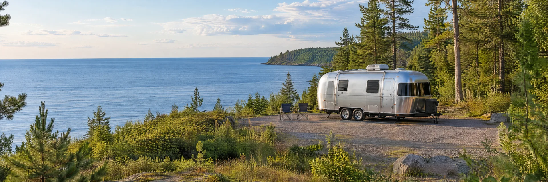 Illustration of a rounded silver travel trailer at a fictional camping setting inspired by Au Train, MI.