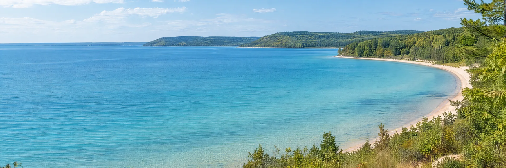 Illustration inspired by Beulah, MI: northwestern Michigan lake country, clear turquoise-blue freshwater lake, pale sandy shore and leafy wooded hills.