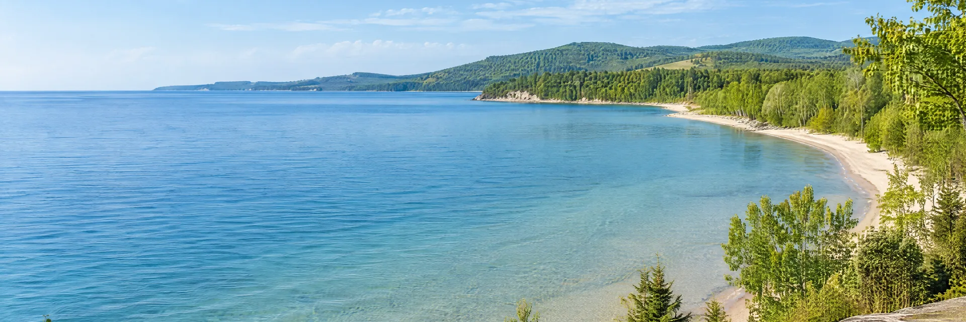 Illustration inspired by Charlevoix, MI: northern Michigan lake country, clear blue water, pale sandy shoreline and leafy hardwood trees with gently rolling green hills.