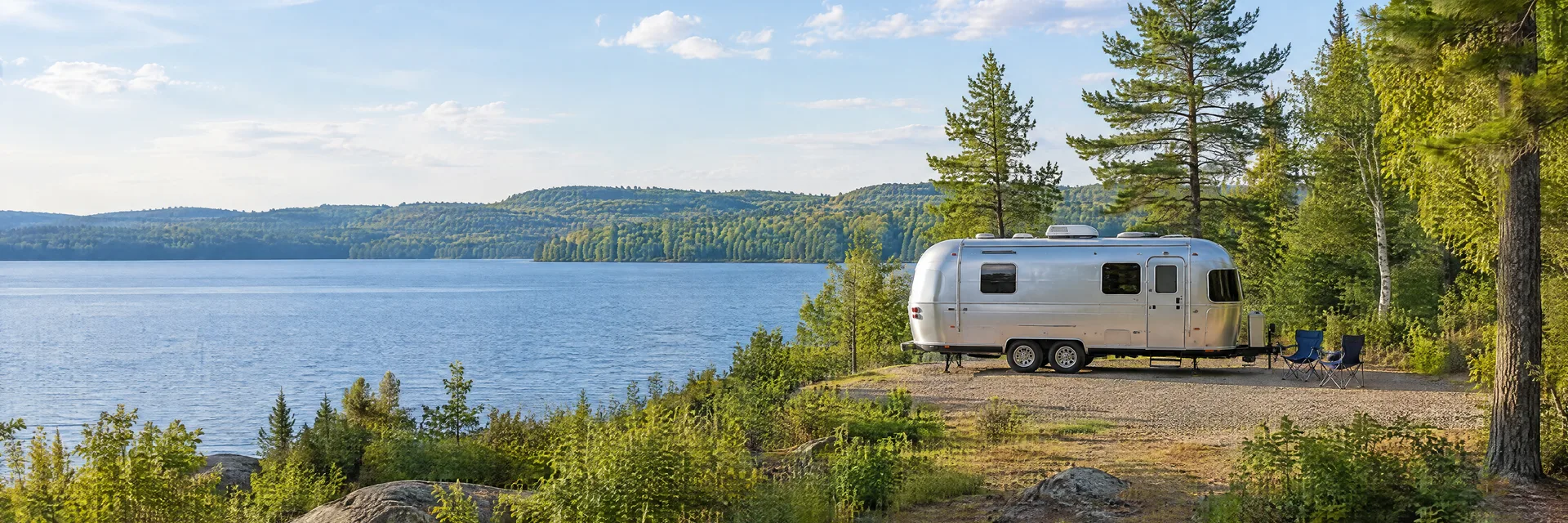 Illustration of a rounded silver travel trailer at a fictional camping setting inspired by Idlewild, MI.