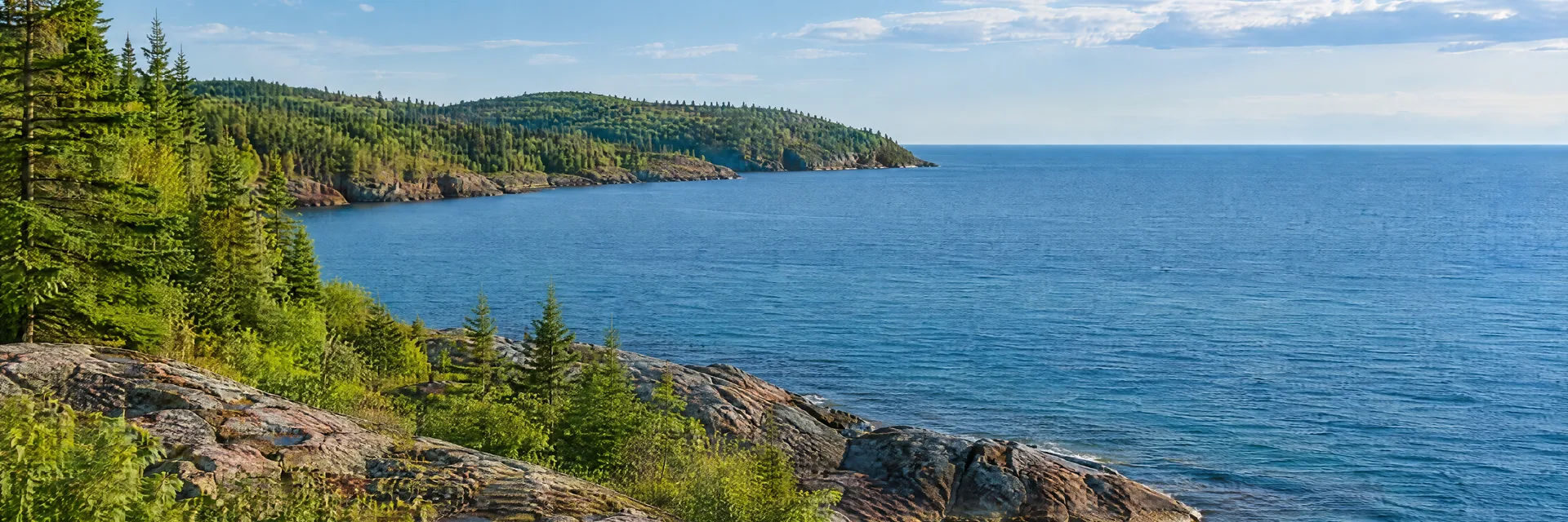 Illustration inspired by Marquette, MI: lake Superior rocky shoreline with forested headland and broad blue horizon.