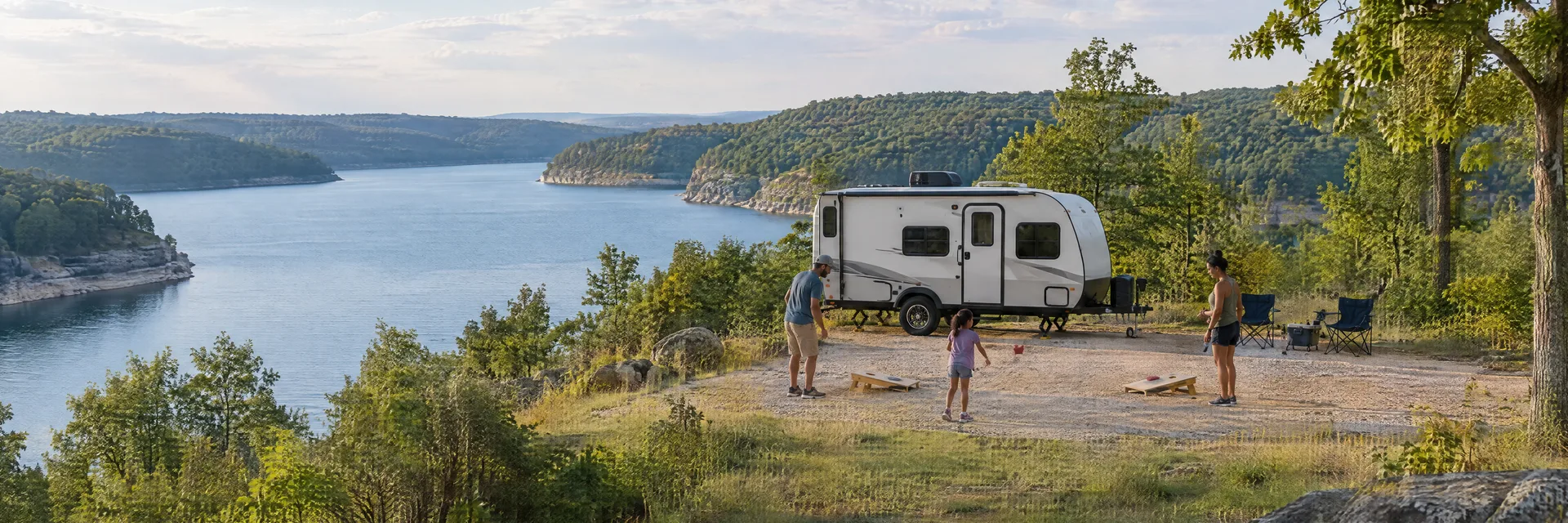 Illustration of campers enjoying family campsite activities beside a compact travel trailer in a fictional camping setting inspired by Piedmont, MO.