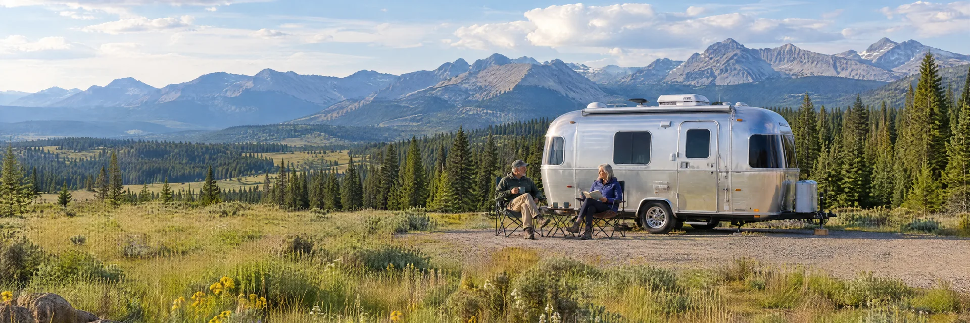 Illustration of campers enjoying relaxing at camp beside a rounded silver travel trailer in a fictional camping setting inspired by Big Sky, MT.