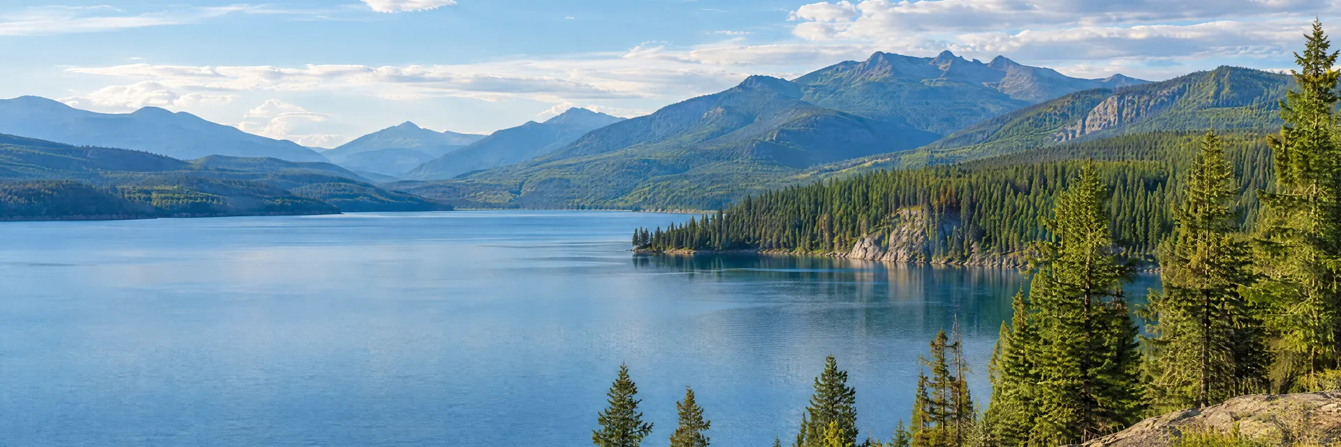 Illustration inspired by Hungry Horse, MT: northwestern Montana reservoir edged by dense conifers and distant forested mountain ridges.