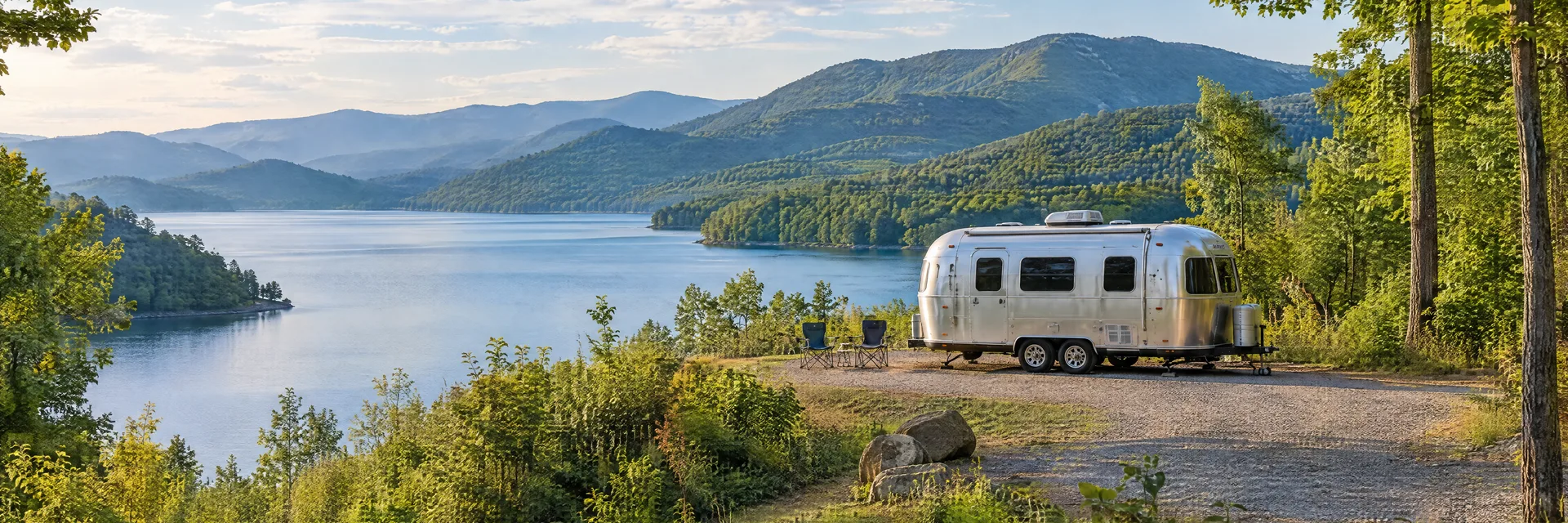 Illustration of a rounded silver travel trailer at a fictional camping setting inspired by Lake Lure, NC.