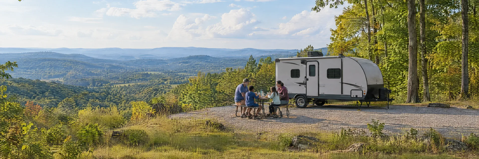 Illustration of campers enjoying a family picnic beside a compact travel trailer in a fictional camping setting inspired by Mount Airy, NC.