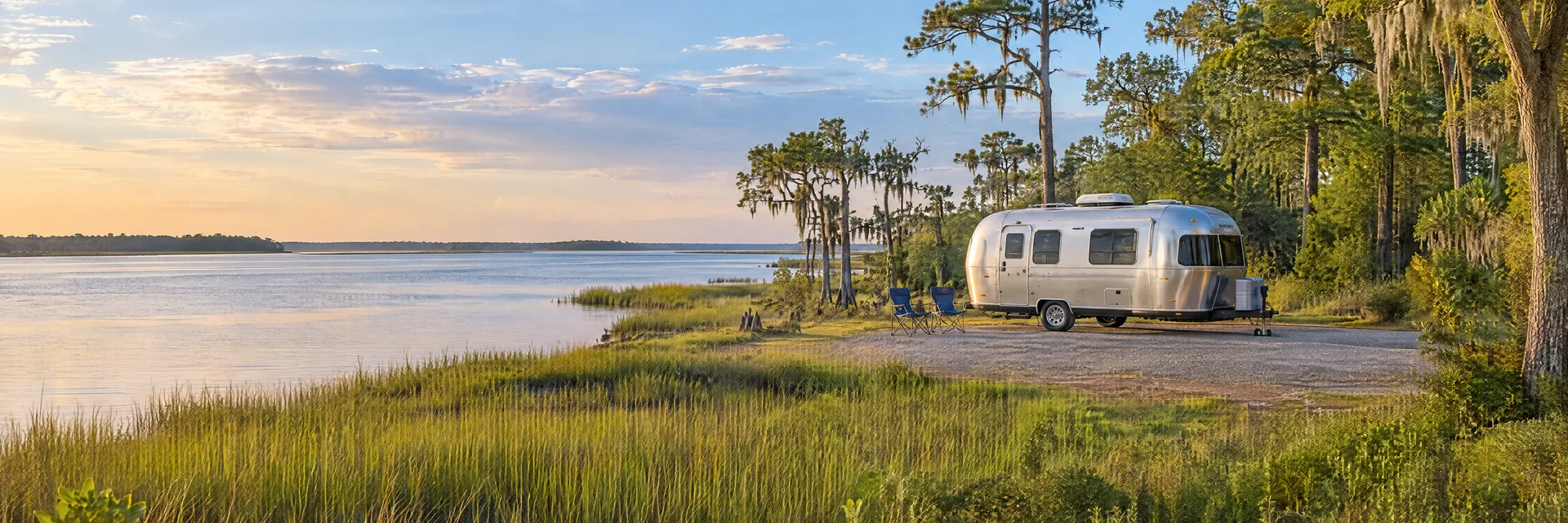 Illustration of a rounded silver travel trailer at a fictional camping setting inspired by New Bern, NC.