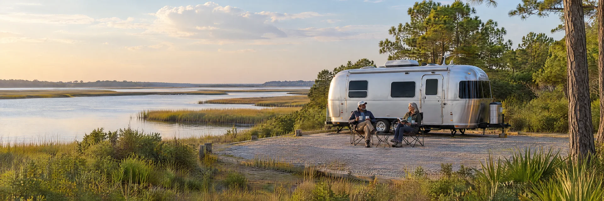 Illustration of campers enjoying relaxing at camp beside a rounded silver travel trailer in a fictional camping setting inspired by Wilmington, NC.