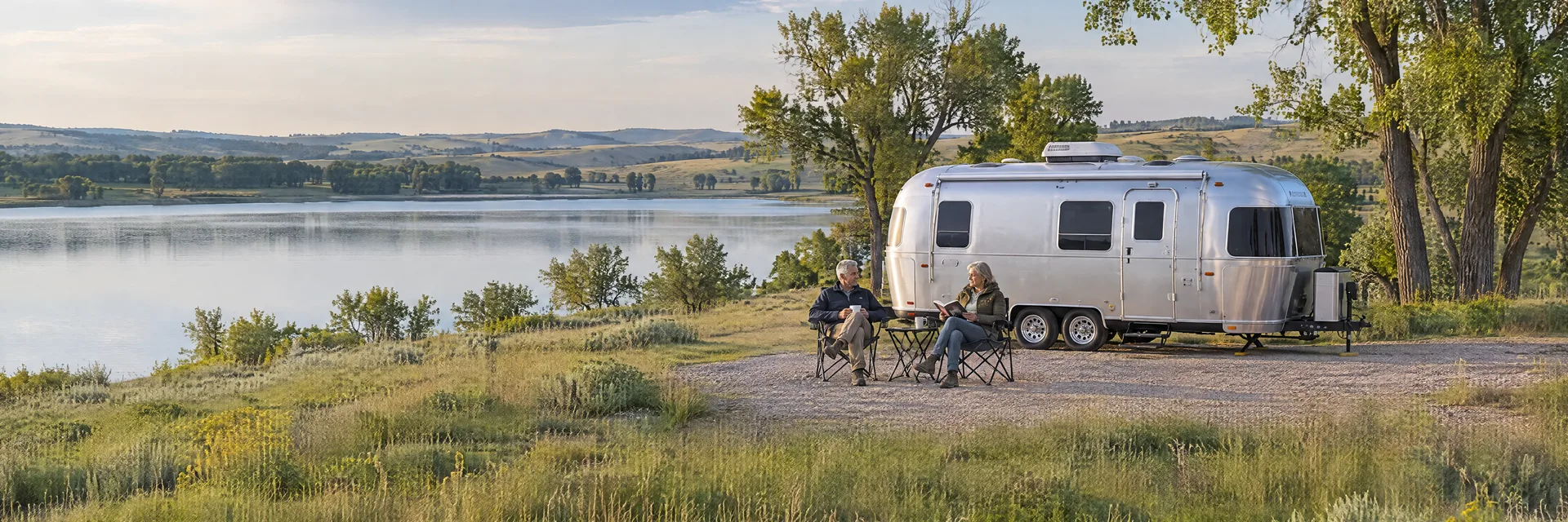 Illustration of campers enjoying relaxing at camp beside a rounded silver travel trailer in a fictional camping setting inspired by La Vista, NE.