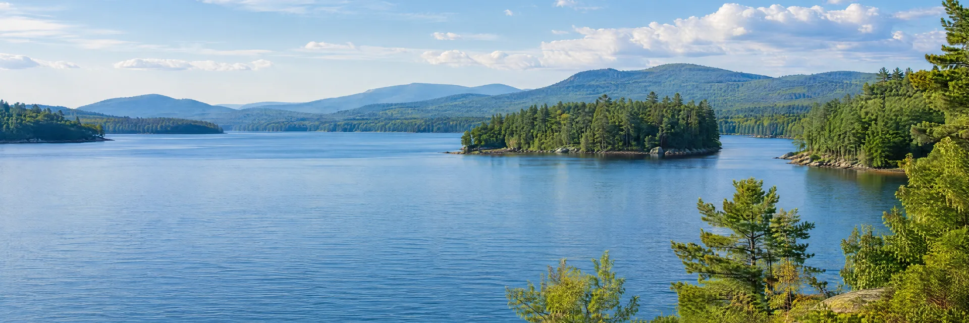 Illustration inspired by Wolfeboro, NH: central New Hampshire lake region, broad blue water, wooded shoreline and softly layered forested hills.