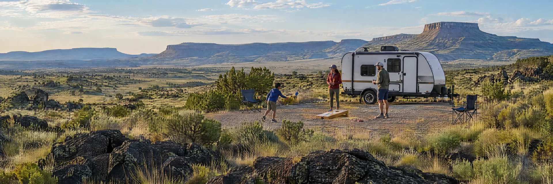 Illustration of campers enjoying family campsite activities beside a compact travel trailer in a fictional camping setting inspired by Grants, NM.