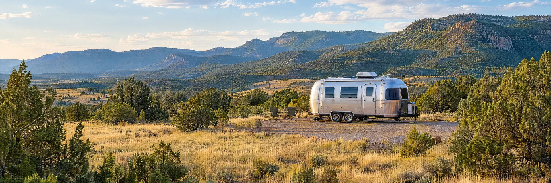 Illustration of a rounded silver travel trailer at a fictional camping setting inspired by Las Vegas, NM.