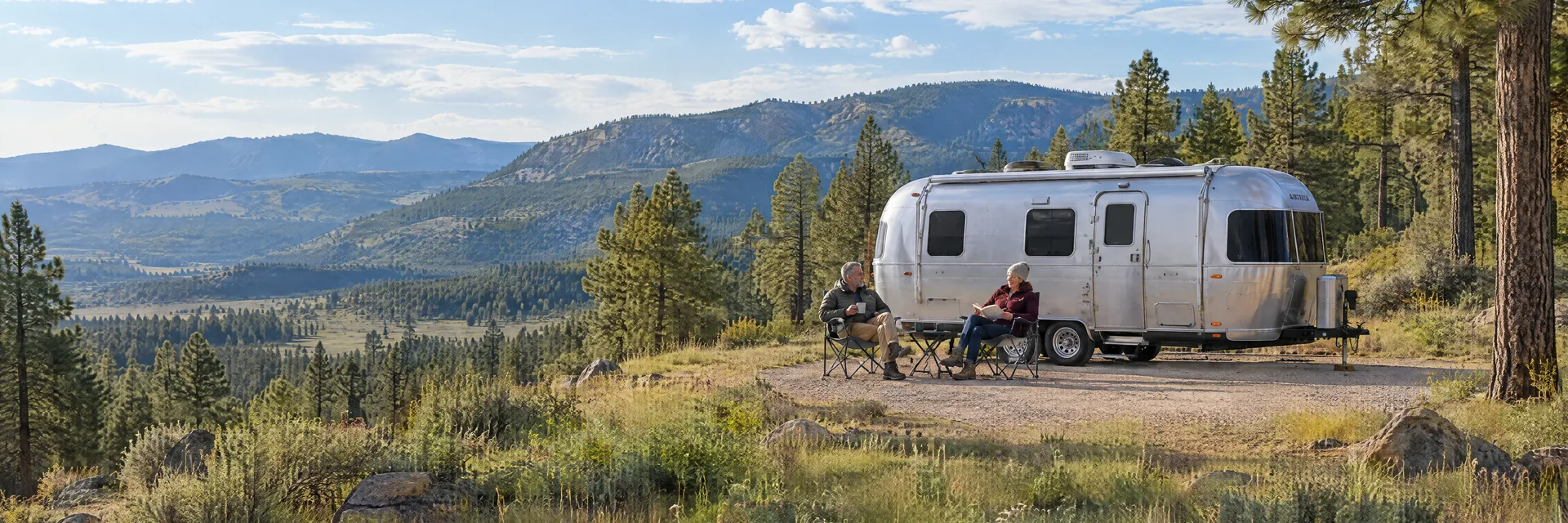 Illustration of campers enjoying relaxing at camp beside a rounded silver travel trailer in a fictional camping setting inspired by Twin Forks, NM.