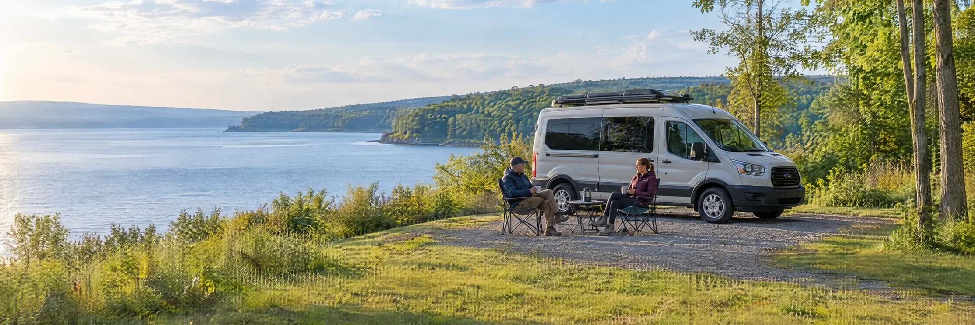 Illustration of campers enjoying morning coffee beside a camper van in a fictional camping setting inspired by Wolcott, NY.