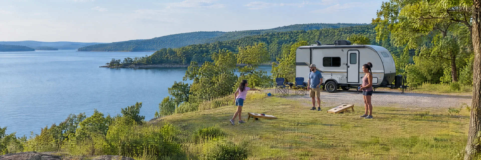 Illustration of campers enjoying family campsite activities beside a compact travel trailer in a fictional camping setting inspired by Grove, OK.