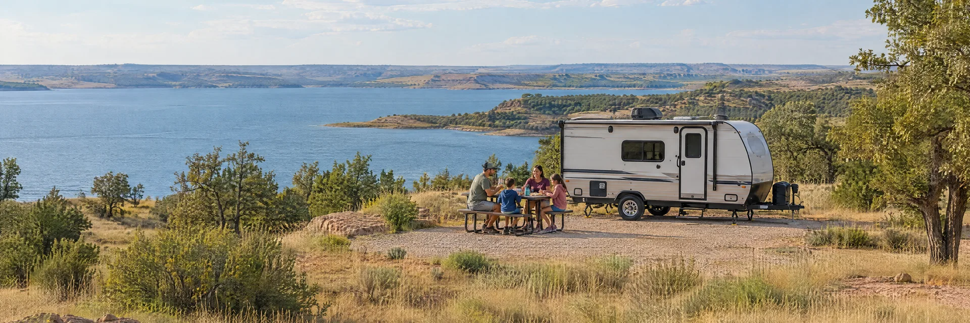 Illustration of campers enjoying a family picnic beside a compact travel trailer in a fictional camping setting inspired by Waurika, OK.