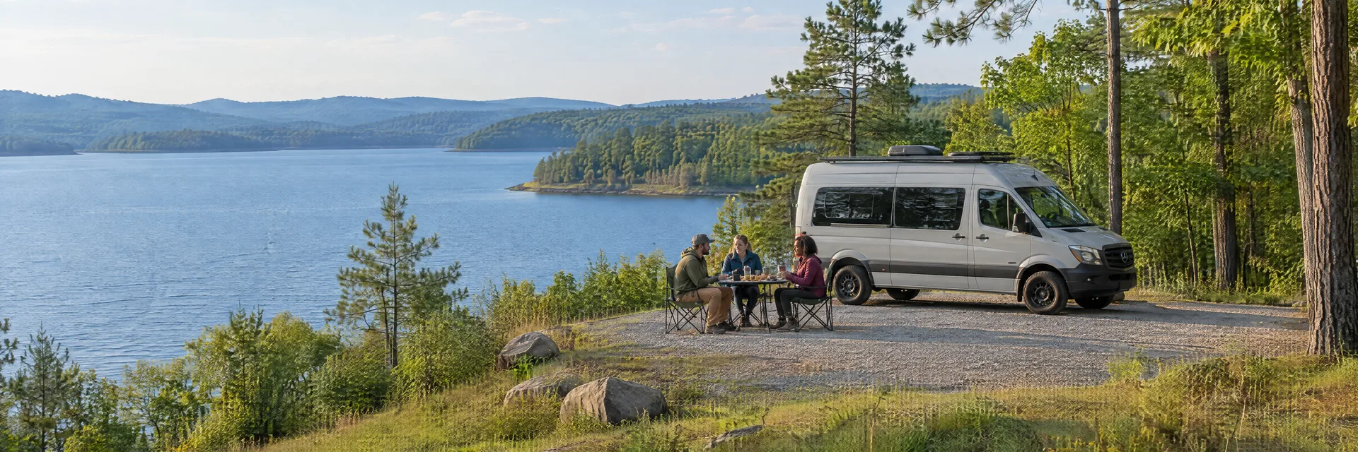 Illustration of campers enjoying an outdoor meal beside a camper van in a fictional camping setting inspired by Mount Carmel, SC.