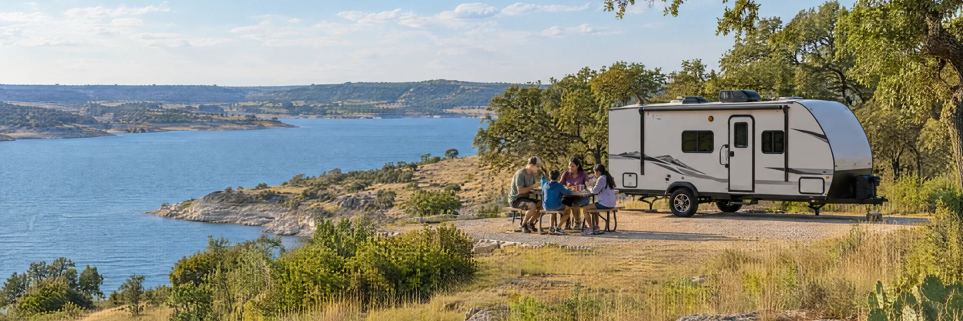 Illustration of campers enjoying a family picnic beside a compact travel trailer in a fictional camping setting inspired by Brownwood, TX.