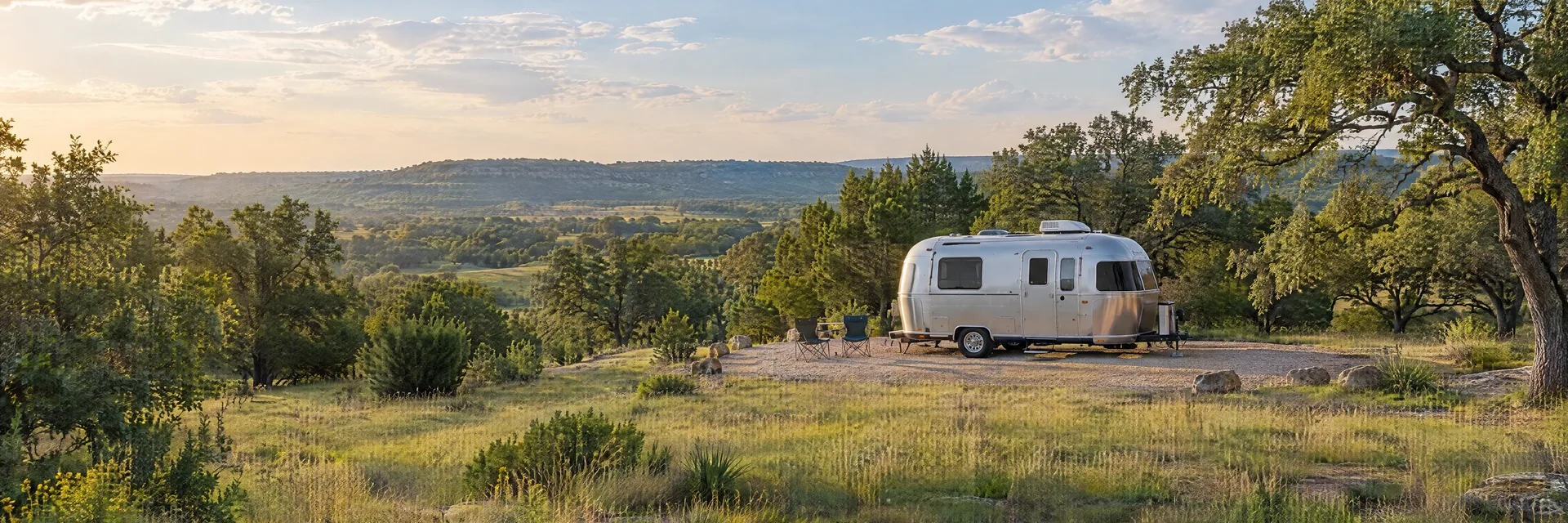 Illustration of a rounded silver travel trailer at a fictional camping setting inspired by Cedar Creek, TX.