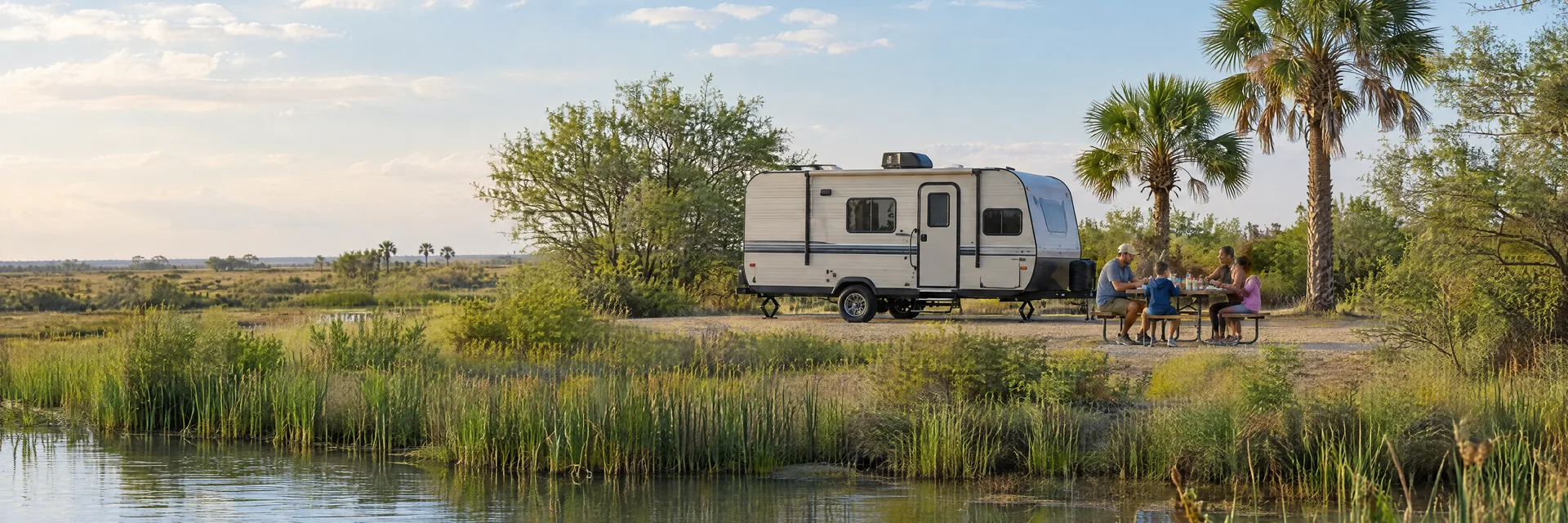 Illustration of campers enjoying a family picnic beside a compact travel trailer in a fictional camping setting inspired by Harlingen, TX.