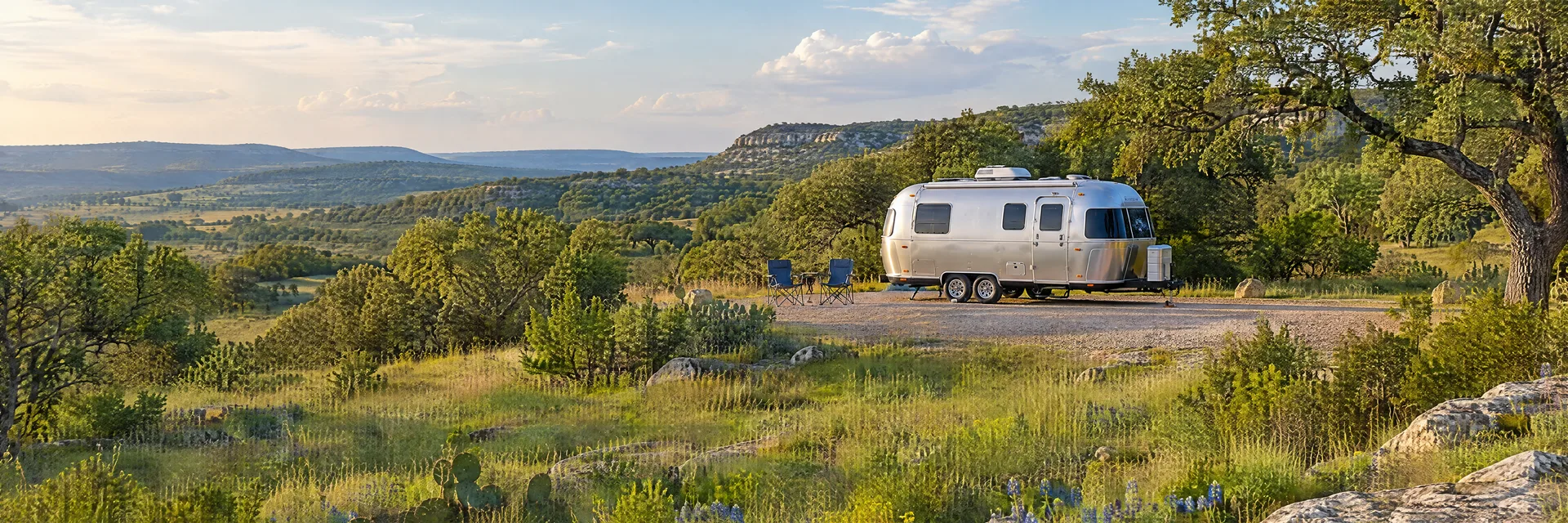 Illustration of a rounded silver travel trailer at a fictional camping setting inspired by Johnson City, TX.