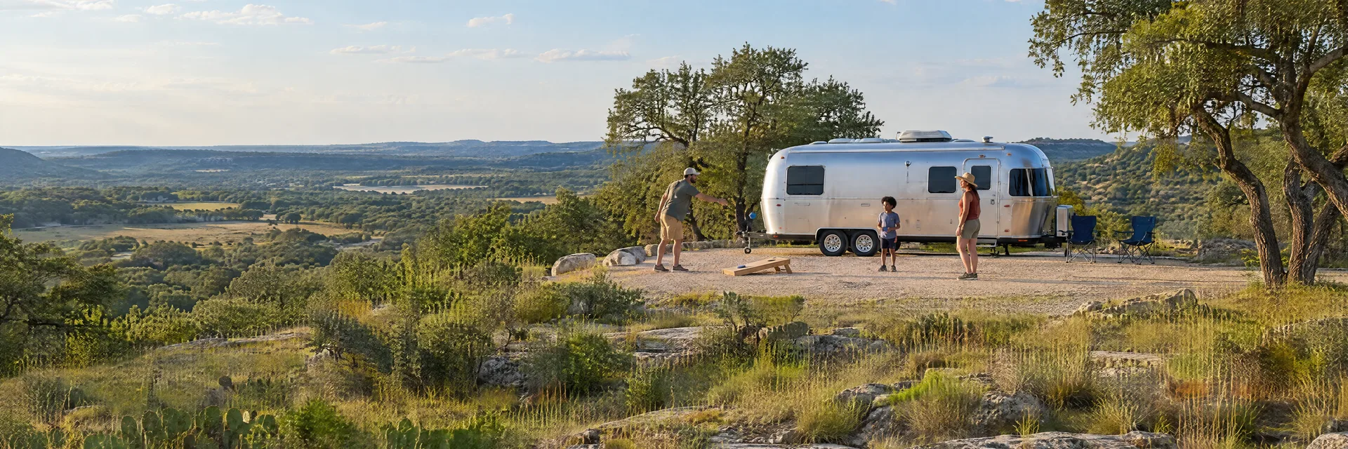 Illustration of campers enjoying family campsite activities beside a rounded silver travel trailer in a fictional camping setting inspired by Lampasas, TX.