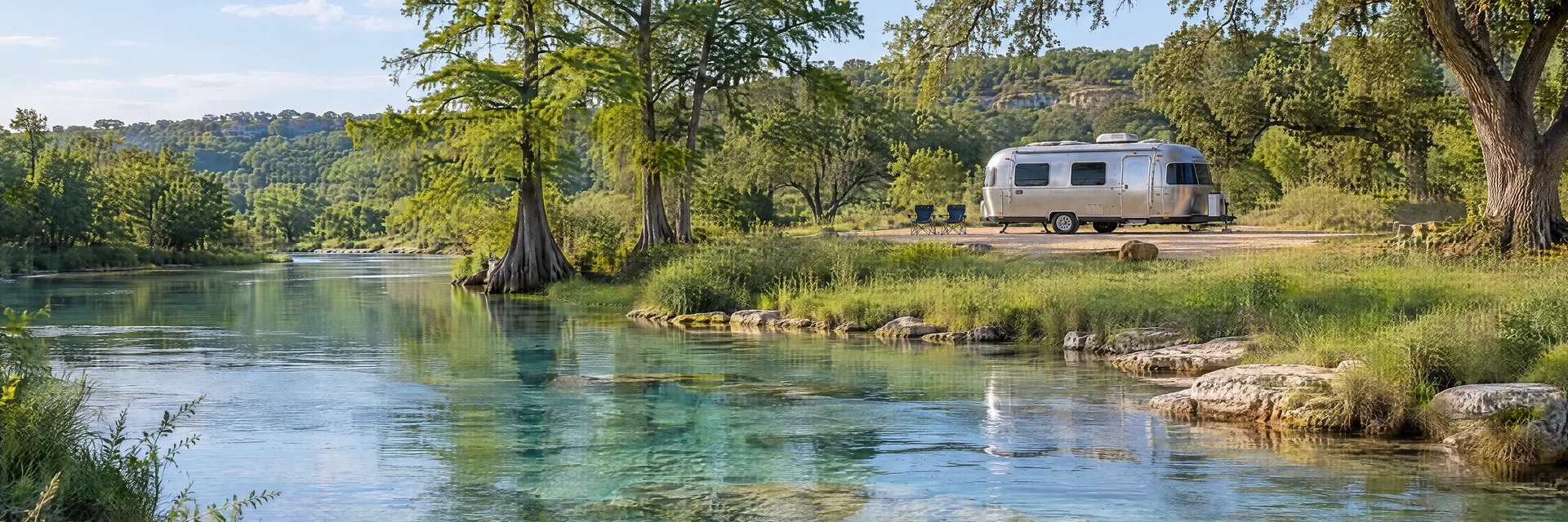 Illustration of a rounded silver travel trailer at a fictional camping setting inspired by San Marcos, TX.